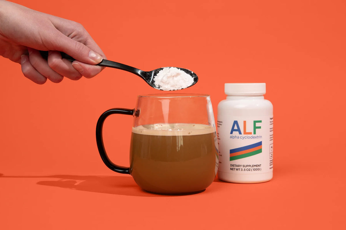 A hand adding a scoop of ALF powder into a mug of coffee